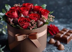 Czekoladki obok czerwonych róż w pudełku z kokardą