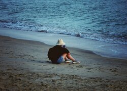 Dziewczyna w kapeluszu siedząca na plaży